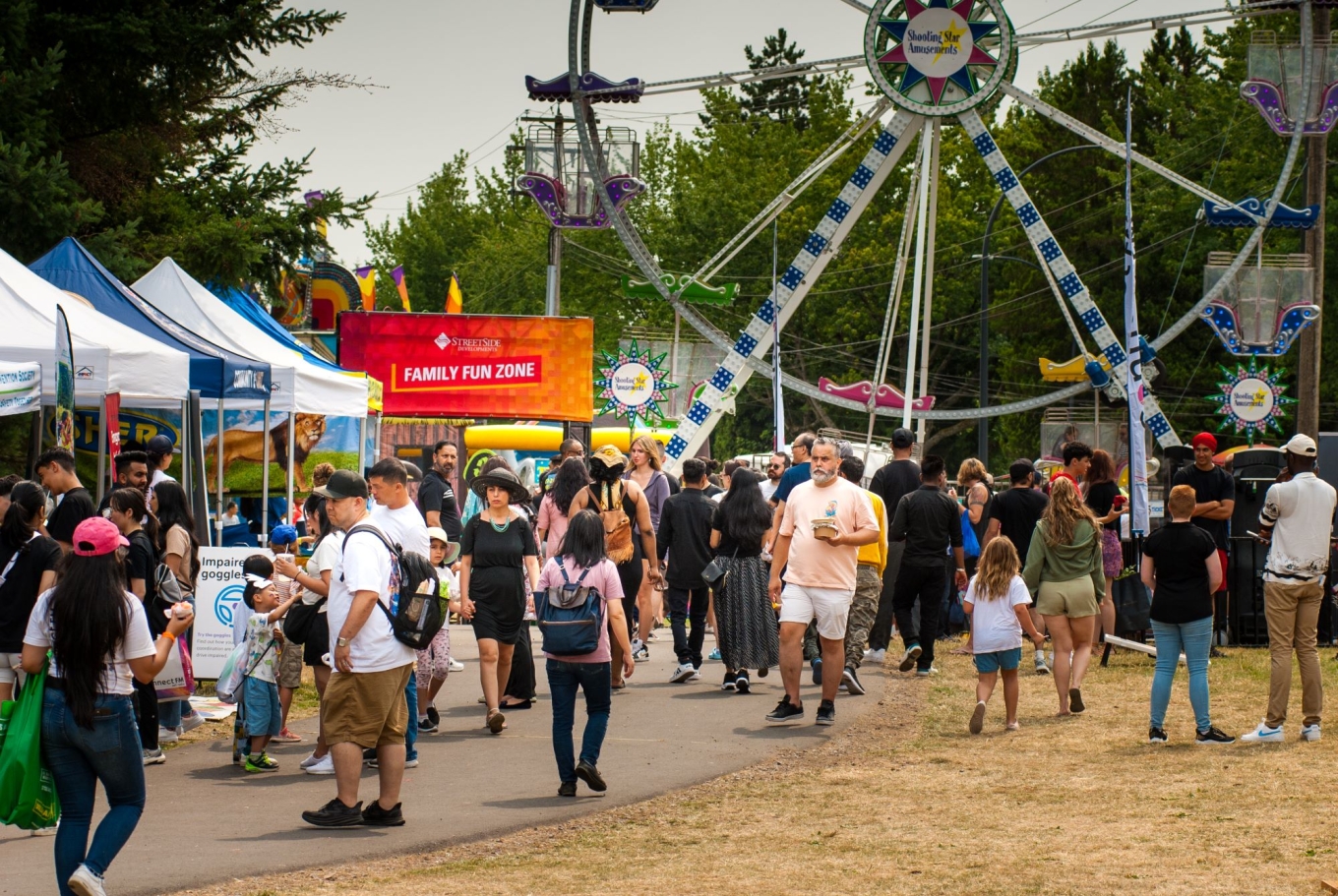 A crowd of people at an event with a Ferris wheel in the background.